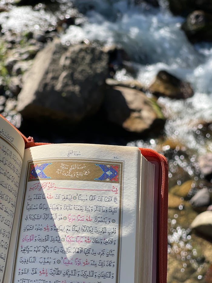 An open Quran with Arabic script by a natural stream, capturing peaceful outdoor ambiance.