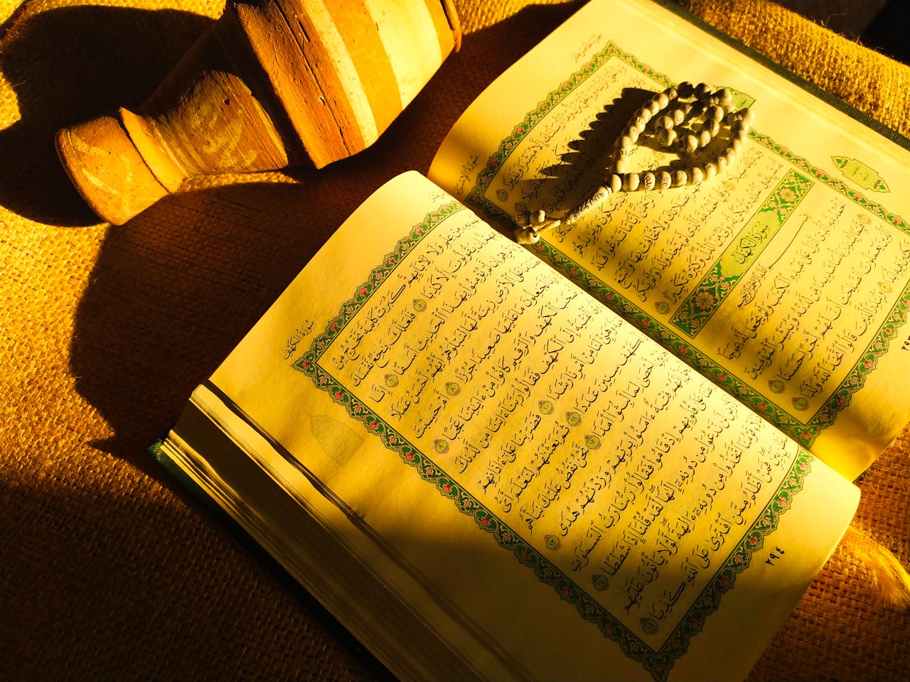 An open Quran with prayer beads and pottery, bathed in warm sunlight. Perfect for religious or cultural content.