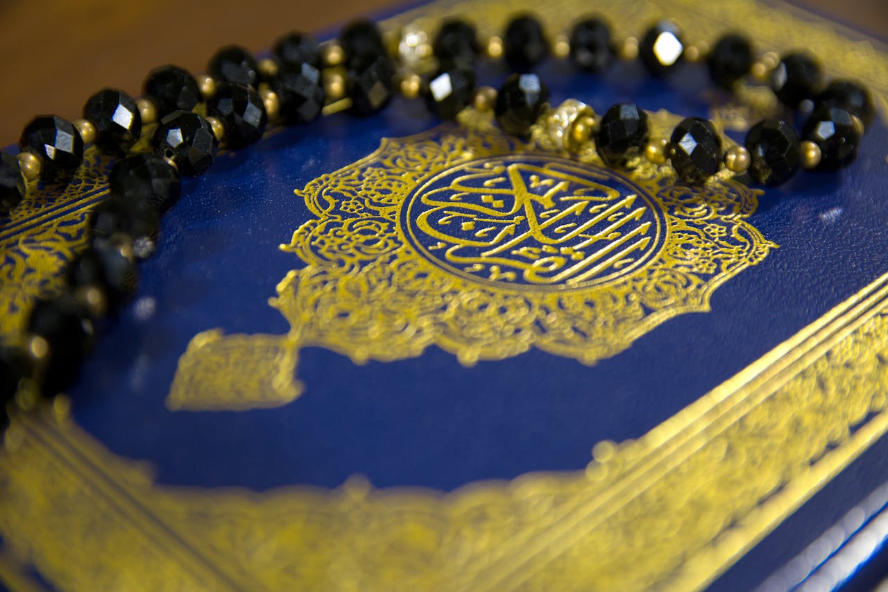 gallery-img-02 Close-up image of the Quran with black prayer beads on a blue cover, symbolizing Islamic faith.
