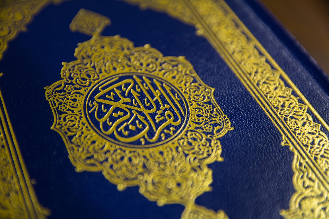 gallery-img-04 Elegant close-up view of the Quran's gold-embossed Arabic calligraphy on a blue cover.