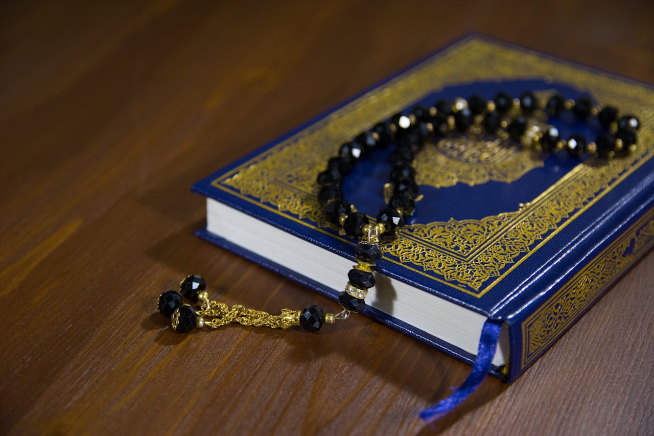 gallery-img-05 Islamic holy book, Quran, with black prayer beads on a wooden table, symbolizing faith and spirituality.
