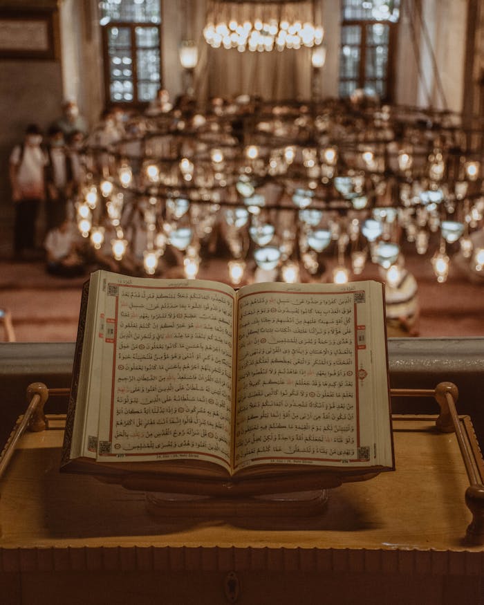 An open Quran displayed on a wooden stand inside a mosque with warm lighting.