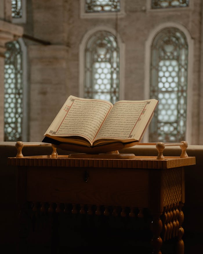 hero-gallery-01 Open Quran on a decorative wooden stand within a mosque, showcasing spiritual ambiance.